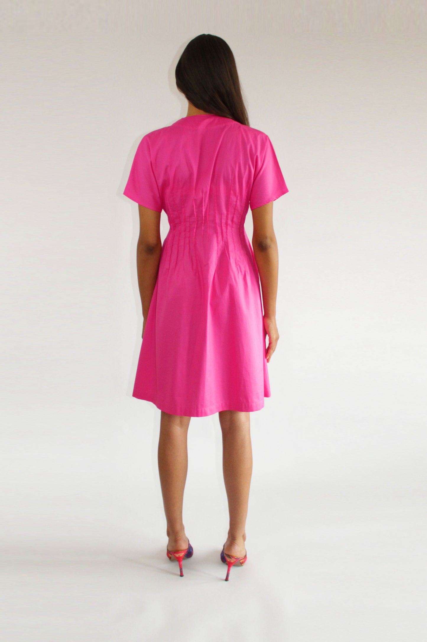 Pink cotton day dress by COLUCCI, crafted from sustainable designer-sourced deadstock fabric. Made-to-order in our London studio, featuring a tailored fit with snap-front closures and a pin-tuck waist for elegance. Ideal for sunny brunches or weekday errands, combining style and comfort.
