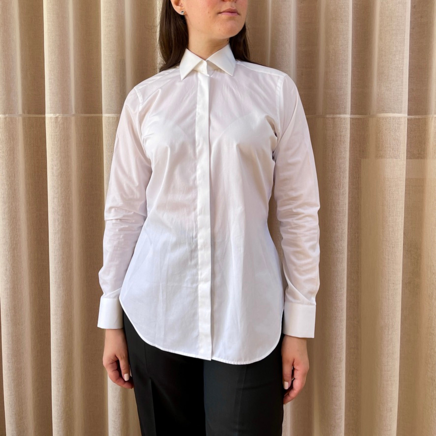 White dress shirt for women by COLUCCI, featuring a wide cutaway collar and concealed placket for refined sophistication. Unique concealed buttons on the collar and cuffs add modern flair, with each button crafted from mother of pearl for a luxurious touch. Made-to-order by our Savile Row tailor, ensuring a perfect fit tailored to the customer’s measurements.