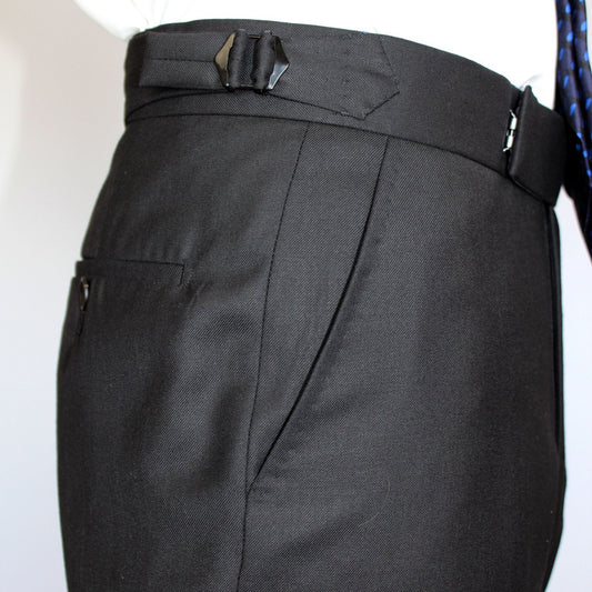 High-waisted tapered trousers by COLUCCI, expertly crafted by a Savile Row tailor from luxurious superfine merino wool with natural stretch. Featuring side adjusters for a perfect fit and a versatile jet-black hue, suitable for both office and casual wear.