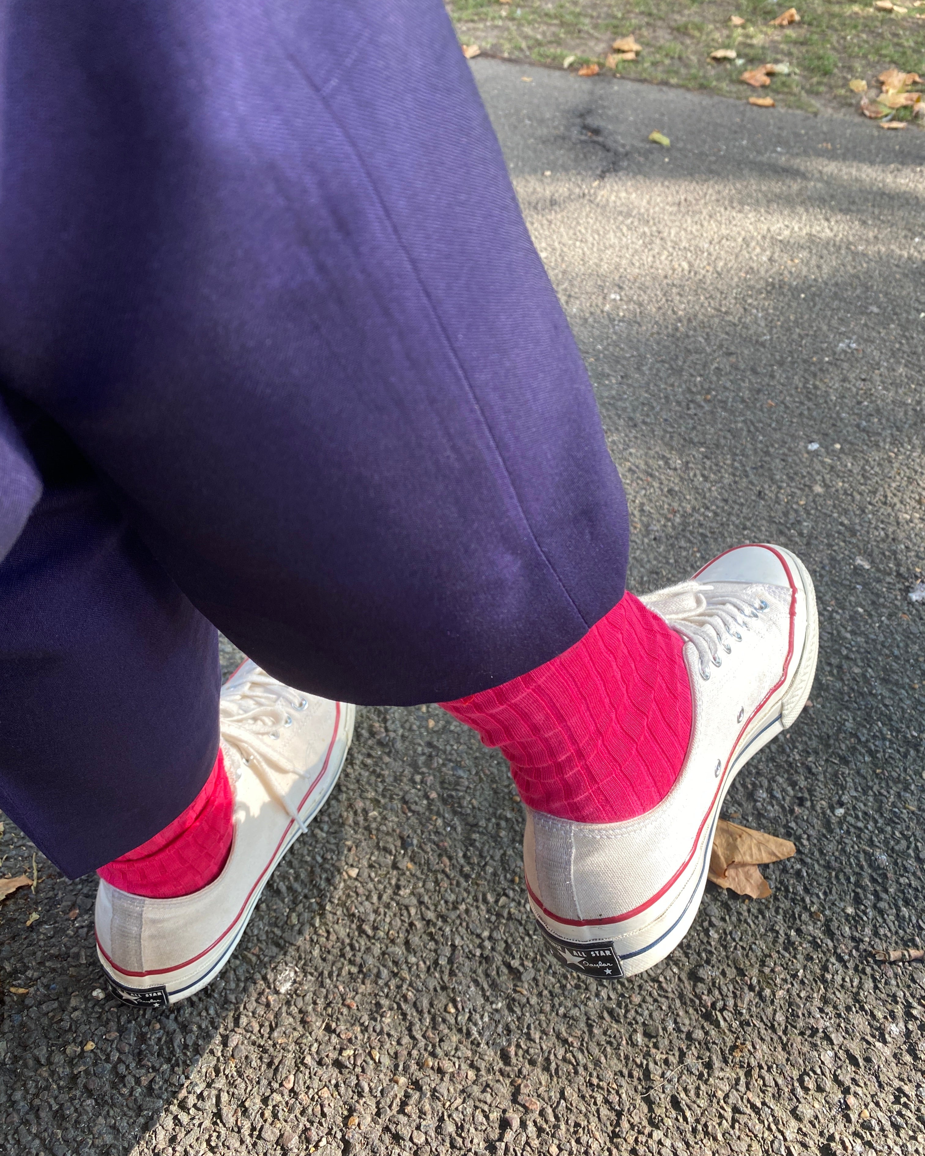 White sneakers with red soles worn on a person's feet, standing on a road.